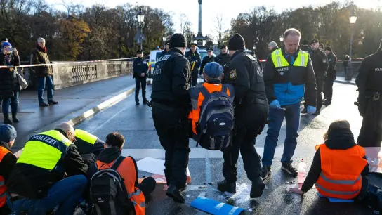 Polizisten tragen in München einen Klimaaktivisten der „Letzten Generation“ weg, der sich zuvor auf der Prinzregentenstraße auf den Asphalt geklebt hatte. (Foto: Lennart Preiss/dpa)