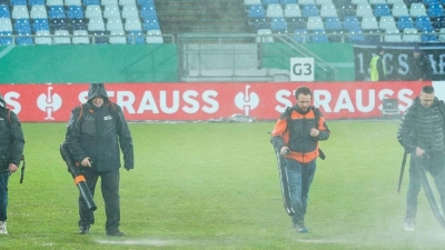Im Ludwigspark-Stadion versuchen Helfer, Wasserlachen vom Spielfeld zu entfernen. (Foto: Uwe Anspach/dpa)