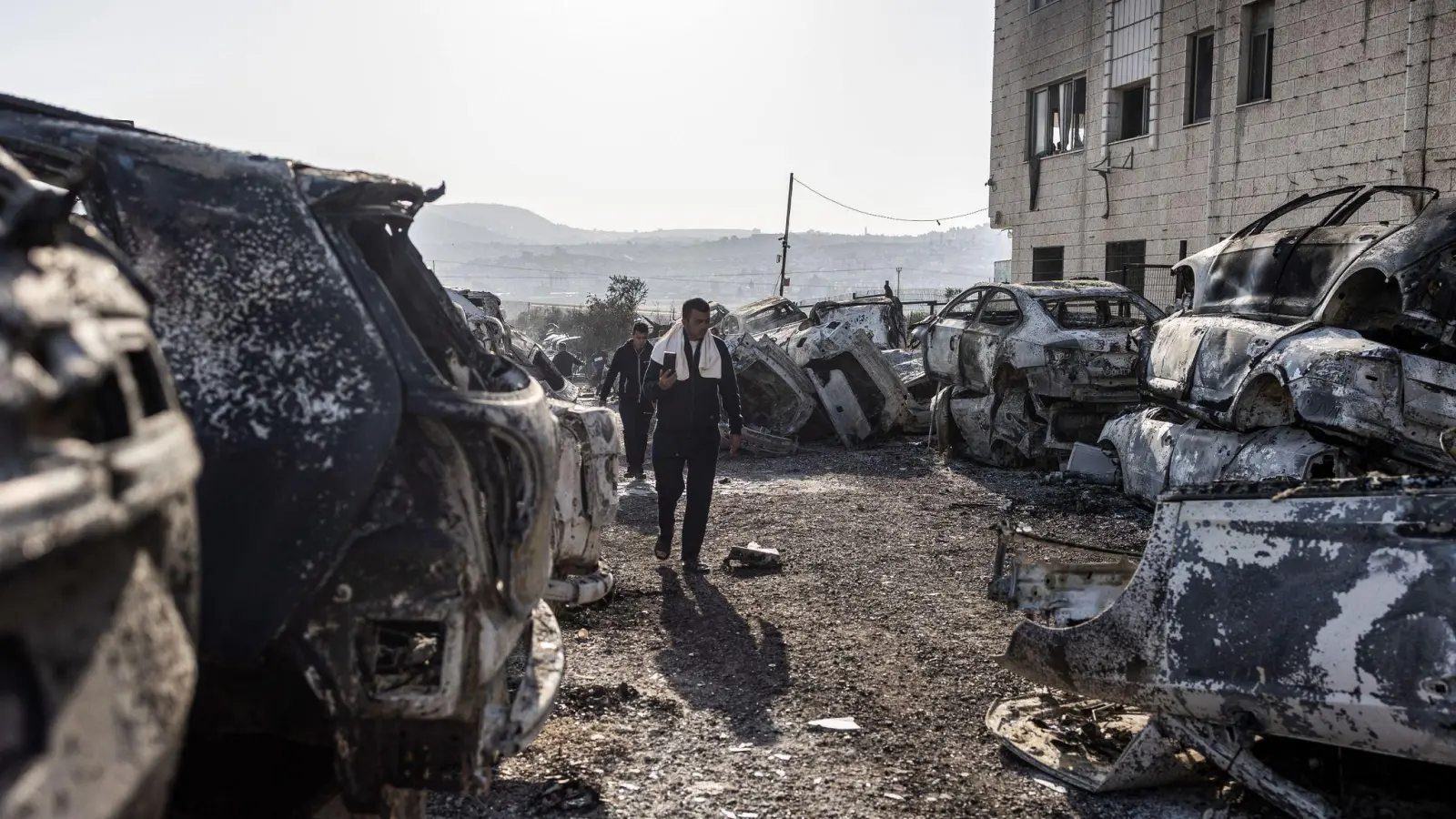 Männer gehen in Huwara an verbrannten und zerstörten Fahrzeugen vorbei. Nach einem tödlichen Anschlag auf zwei Israelis war es dort zu schweren Ausschreitungen israelischer Siedler gekommen. (Foto: Ilia Yefimovich/dpa)