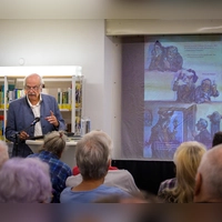 Karl-Heinz Röhlin liest in der Gemeindebücherei Neuendettelsau aus seiner fränkischen Fassung des „Brandner Kaspar”. Auf der Leinwand hinter ihm laufen die Zeichnungen von Jan Reiser mit. (Foto: René Chlopotowski)
