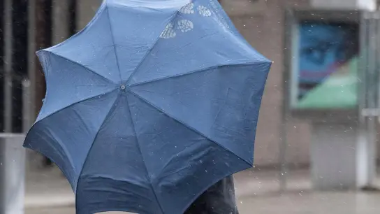 Bei Regenwetter kämpft sich ein Passant mit Regenschirm durch die Innenstadt. (Foto: Boris Roessler/dpa/Symbolbild)