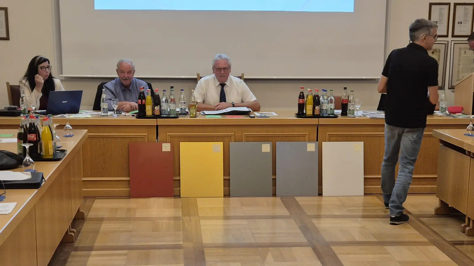 Sichtlich gut gelaunt wartete das Bürgermeister-Trio mit Heike Gareis, Peter Holzmann und Klaus Meier (sitzend von links) auf das Ergebnis der Abstimmung über die am Ratstisch lehnenden Musterplatten, nachdem Bauamtsleiter Gerald Schorr (rechts) die Stimmzettel verteilt hatte.  (Foto: Patrick Lauer)