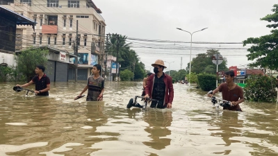 Anwohner schieben ihre Fahrräder durch eine überschwemmte Straße in Bago. (Foto: Thein Zaw/AP/dpa)