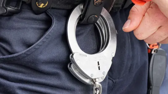 Handfesseln aus Metall hängen am Gürtel eines Polizisten. (Foto: Soeren Stache/dpa)
