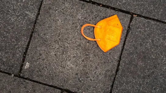 Ein gebrauchter orangefarbener Mund-Nasen-Schutz liegt auf dem Gehweg. (Foto: Peter Kneffel/dpa/Symbolbild)