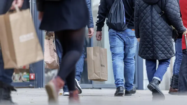 Menschen gehen mit ihren Einkaufstaschen auf einer Straße entlang. (Foto: Markus Scholz/dpa/Symbolbild)
