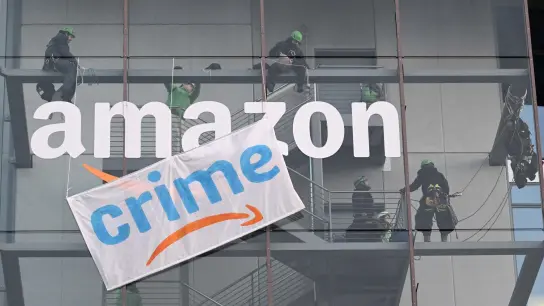 Greenpeace-Aktive hängen während der Rabattaktion Black Friday ein Plakat mit der Aufschrift „crime“ am Amazon Deutschland Gebäude auf. (Foto: Felix Hörhager/dpa)