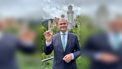 Finanzminister Albert Füracker (CSU)&nbsp;mit dem „Bayern Thaler“ in der Hand vor Schloss Neuschwanstein. (Foto: -/Bayerisches Finanzministerium/dpa)