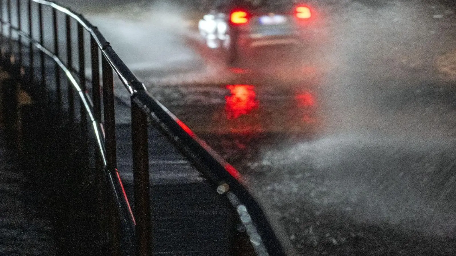 Wasser spritzt, während Fahrzeuge über eine überschwemmte Straße fahren. (Foto: Pia Bayer/dpa)