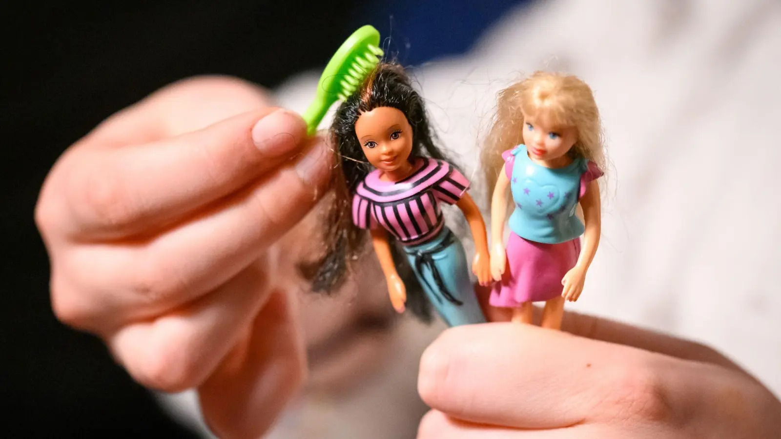 Eine junge Frau kämmt die Haare von zwei der größeren Polly Pocket Puppen. (Foto: Jonas Walzberg/dpa)