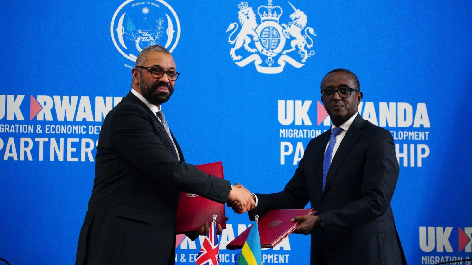 Großbritanniens Innenminister James Cleverly (l) und Vincent Birut, Außenminister von Ruanda, schütteln sich die Hände. Mit dem neuen Vertrag will die britische Regierung Asylsuchende künftig in das ostafrikanische Land abschieben. (Foto: Ben Birchall/Pool PA/AP/dpa)