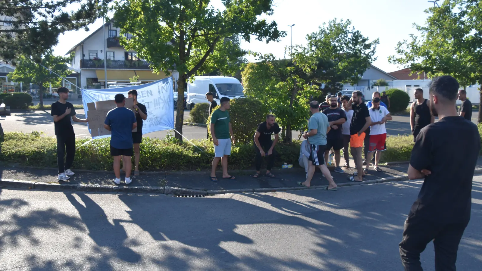 An der Kreuzung nahe der Scheinfelder Notunterkunft (rechts im Hintergrund) demonstrierten rund zwei Dutzend Bewohner gegen die Zustände im Lager. „Wir leben in Krankheit“, steht auf dem zwischen den Bäumen hängenden Transparent samt einem Hilferuf an die Weltgesundheitsorganisation. (Foto: Andreas Reum)