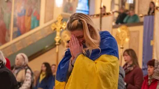 Eine Frau mit einer ukrainischen Flagge nimmt am Auferstehungsgottesdienst teil. (Foto: Peter Kneffel/dpa)