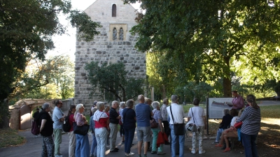 Pfarrer Dr. Oliver Gußmann (rechts, vor dem Schild stehend) erklärte den Teilnehmenden im Burggarten zuerst draußen etwas über die Blasiuskapelle, die im Hintergrund zu sehen ist. Anschließend ging es dann nach innen. (Foto: Anna Beigel)