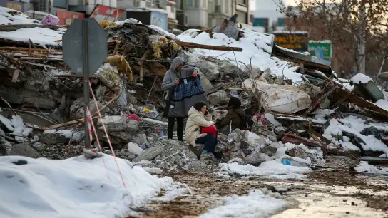 Menschen sitzen zwischen den Trümmern vor einem eingestürzten Gebäude. (Foto: Emrah Gurel/AP/dpa)