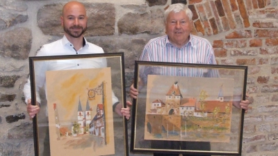 Die Stiftsbasilika und der Storchenturm in Aquarell: Diese beiden Bilder, die Herriedens Bürgermeister Patrick Peters (links) und Altbürgermeister Werner Herzog präsentieren, gehören zur Sammlung, die die Stadt nun ihr Eigen nennen darf. (Foto: Jasmin Kiendl)