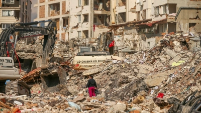 Ein Mann steht in Samandag in der Türkei zwischen Trümmern, während Bagger die Überreste eines zerstörten Gebäudes abtransportieren. Nach dem katastrophalen Beben am 6.2. kommt es in der Region immer wieder zu Nachbeben. (Foto: Emrah Gurel/AP/dpa)