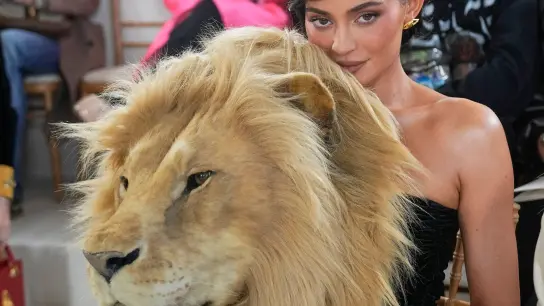 Kylie Jenner hinter einem täuschend echt aussehenden Löwenkopf. (Foto: Michel Euler/AP/dpa)