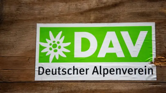 Das Logo des Deutschen Alpenverein (DAV) klebt auf einer Holzbox. (Foto: Lino Mirgeler/dpa/Symbolbild)