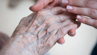 Eine Pflegerin hält die Hand einer Bewohnerin in einem Seniorenzentrum. (Foto: Christophe Gateau/dpa)