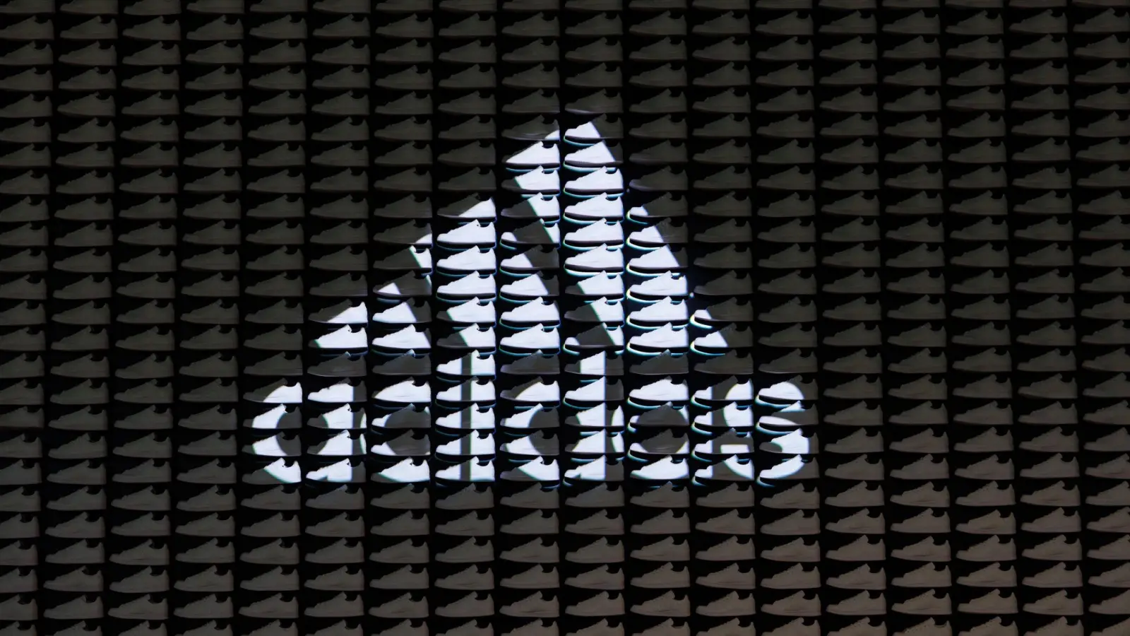 Das Logo der Adidas AG wird auf eine Wand aus Turnschuhen projiziert. (Foto: Daniel Karmann/dpa)