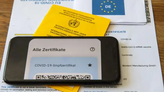 Ein Impfpass und ein Smartphone, auf dem die App CovPass läuft, liegen auf einem Impfzertifikat, das von einer Apotheke ausgestellt wurde. (Foto: Stefan Puchner/dpa/Illustration)