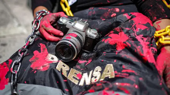 Eine Journalistin und Aktivistin mit einer rot verschmierten Kamera und einer Presseweste bei einer symbolischen Aktion in Mexiko-Stadt. (Foto: Quetzalli Blanco/NOTIMEX/dpa)