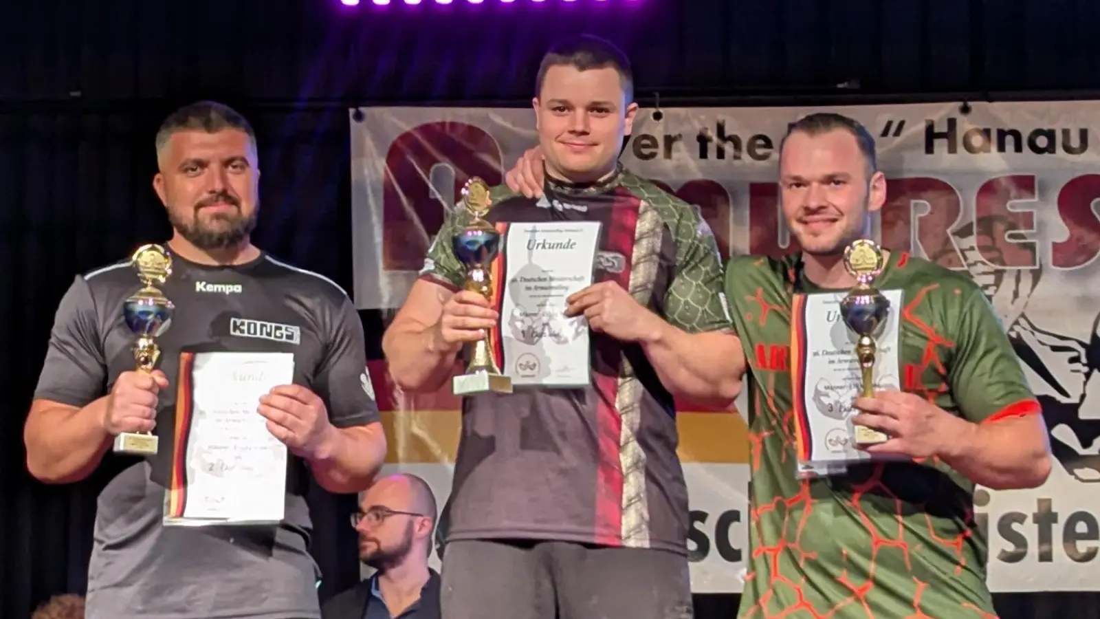 Starke Männer mit Urkunde: Felix Sieghörtner (Mitte) holt bei der DM mit dem linken und dem rechten Arm den Titel. Finalgegner war jeweils Leotrim Bytyqi (links). (Foto: Viola Wurster)