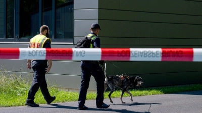Polizeibeamte ermitteln mit einem Spürhund am Schulzentrum in Lohr am Main, wo der tote 14-Jährige gefunden wurde. (Foto: Pia Bayer/dpa)