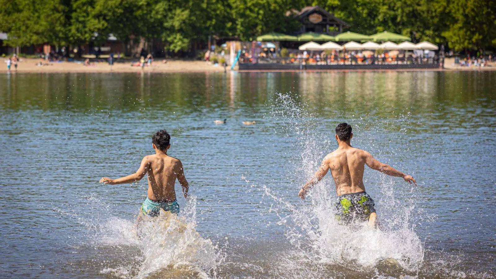 Zwei junge Männer rennen bei sonnigem Wetter in das Wasser eines Sees. (Foto: Moritz Frankenberg/dpa/Symbolbild)
