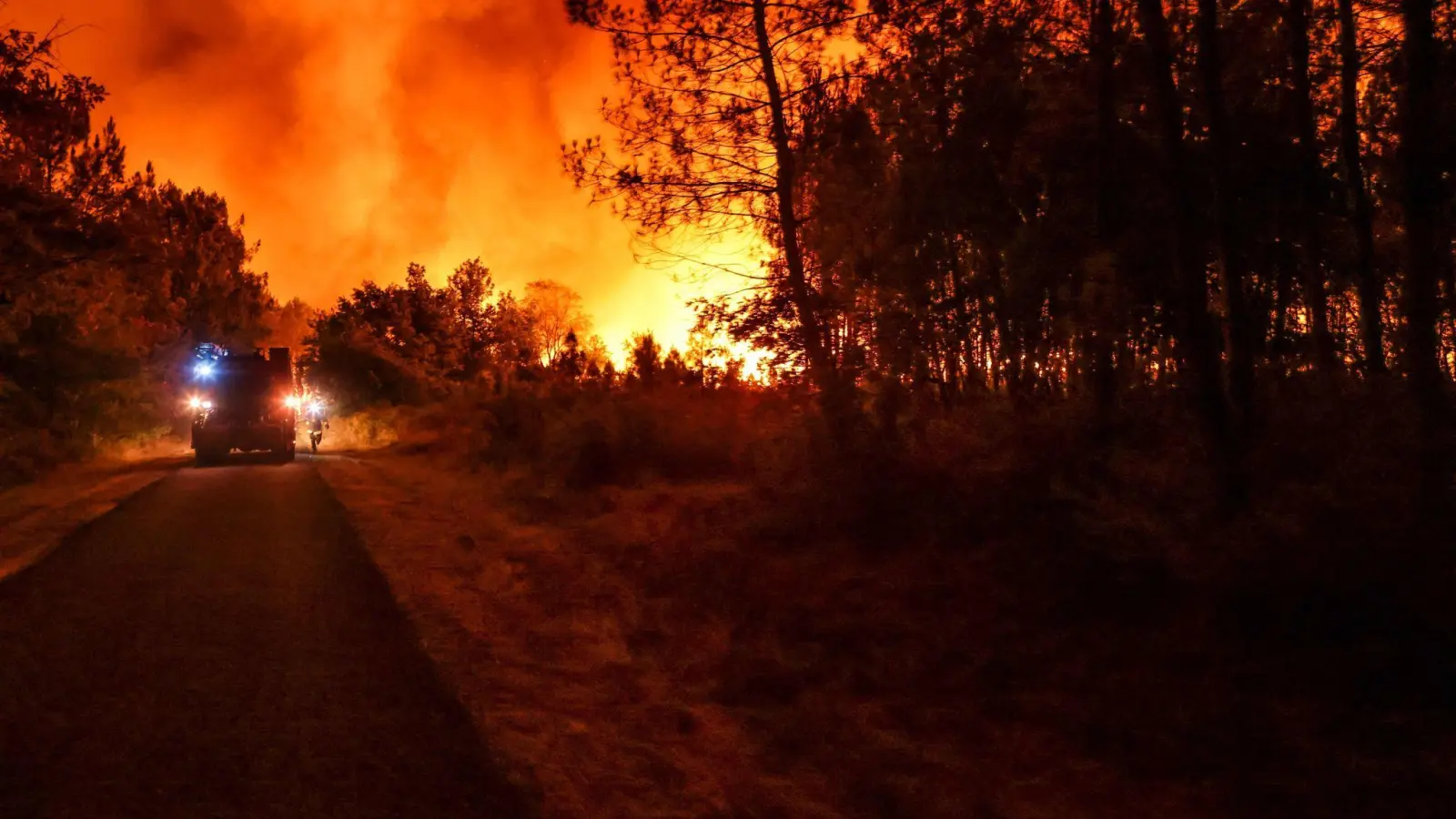 Ein Feuerwehrfahrzeug fährt auf einer Straße an den Flammen eines Waldbrandes in der Nähe von Belin-Beliet vorbei. (Foto: Thibaud Moritz/AFP/dpa)