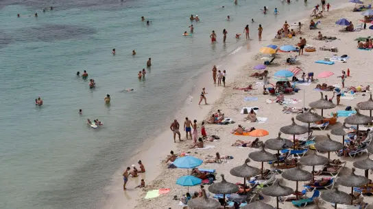 Touristen genießen an einem Strand bei Puerto Portals auf Mallorca die Sonne und das Meer. Der Klimawandel stellt die Reisebranche vor neue Herausforderungen. (Foto: Clara Margais/dpa)