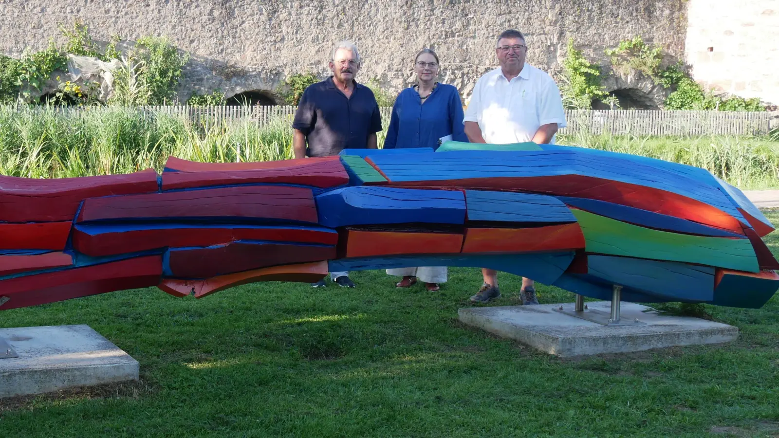 Die Skulptur „Brückenbogen“ erstrahlt wieder in kräftigen Farben. Darüber freuen sich (v.l.) Zweiter Bürgermeister Herbert Argmann, Künstlerin Cornelia Königsperger und Heimatvereins-Vorsitzender Hans Popp. (Foto: Daniel Ammon)