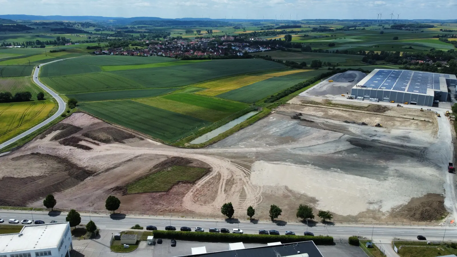 Das Areal, auf dem TransnetBW sein Zentrallager errichtet, gehört zum Gemeindegebiet Gebsattel. Auf der Drohnenaufnahme ist das Dorf im Hintergrund zu erkennen. Links verläuft die Kreisstraße nach Neusitz. Im Vordergrund ist die ins Rothenburger Gewerbegebiet führende Erlbacher Straße zu sehen. Die Halle am rechten Bildrand, die aus dem Bestand des 2024 insolvent gegangenen Küchenplatten-Herstellers Lechner stammt, wird in die neue Nutzung einbezogen. (Foto: Stefan Zeller)