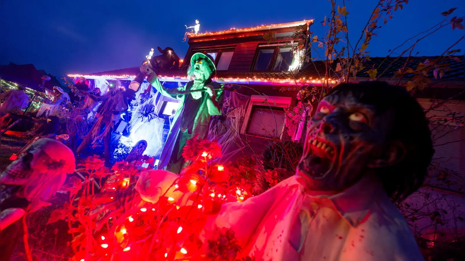 Gruselige Figuren stehen in Mettmann vor einem beleuchteten Halloween-Haus. (Foto: Henning Kaiser/dpa)