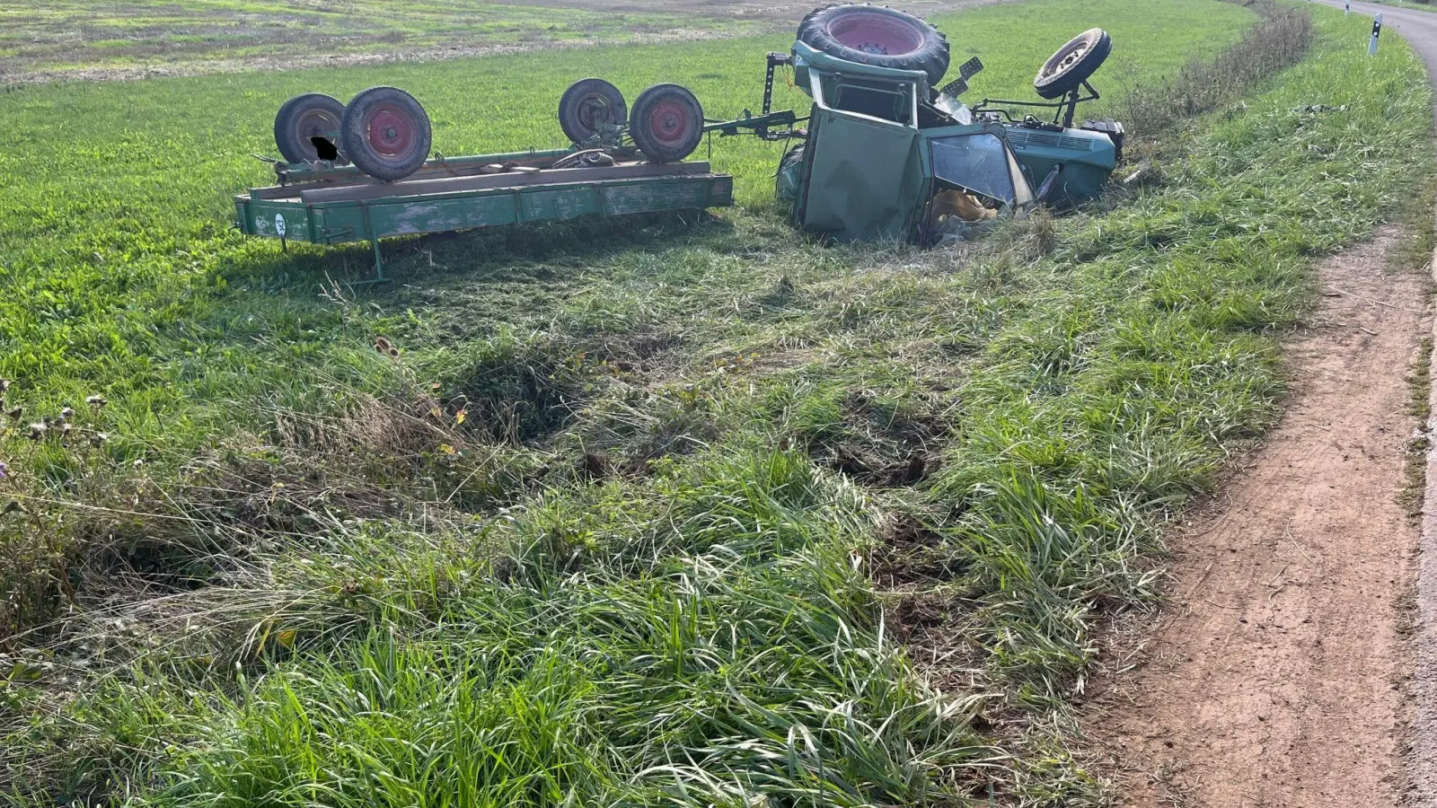 Ein Traktor liegt samt Anhänger in einem Feld. (Foto: -/Polizei Dinkelsbühl/dpa)