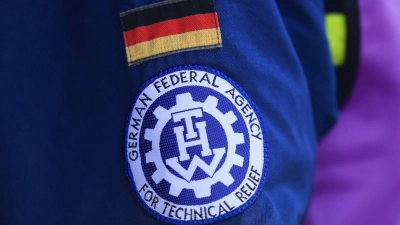 Fahne und Logo des Technischen Hilfswerk (THW) hängen an der Jacke eines Mitarbeiters. (Foto: Oliver Berg/dpa/Symbolbild)