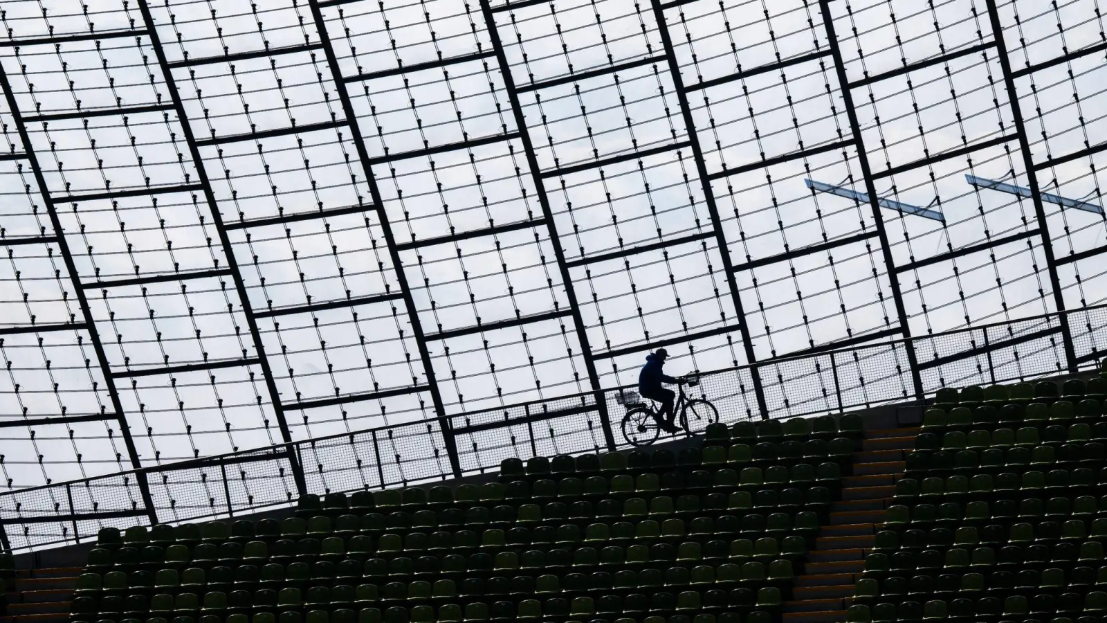 Ein Mitarbeiter des Olympiastadions fährt mit einem Fahrrad am Glasdach der Spielstätte vorbei. (Foto: Peter Kneffel/dpa)