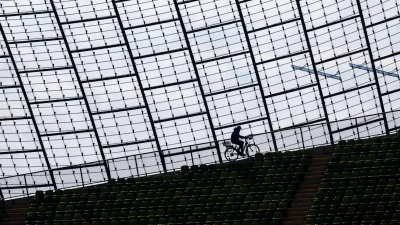 Ein Mitarbeiter des Olympiastadions fährt mit einem Fahrrad am Glasdach der Spielstätte vorbei. (Foto: Peter Kneffel/dpa)