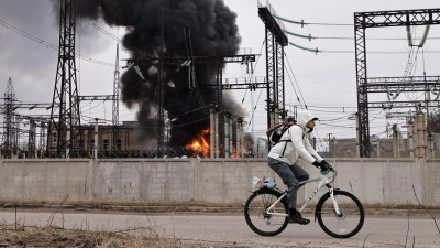 Nach einem russischen Angriff fährt ein Mann mit seinem Rad an einem brennenden Elektrizitätswerk in Charkiw vorbei. (Foto: Yevhen Titov/AP/dpa)