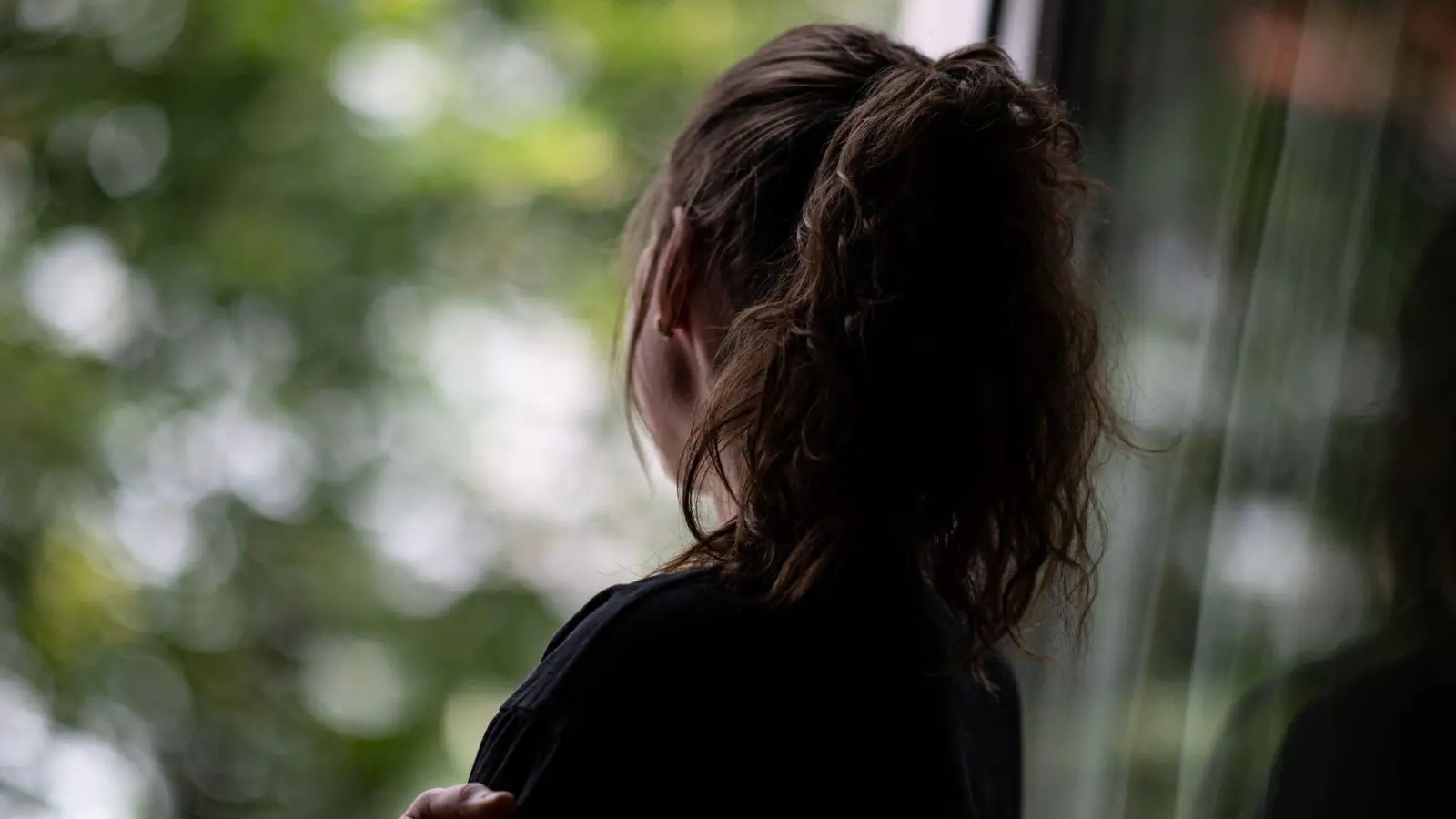Eine Jugendliche steht gedankenversunken am Fenster. Selbstverletzendes Verhalten kann vorübergehend negative Gefühle verdrängen. (Foto: Fabian Sommer/dpa/dpa-tmn)