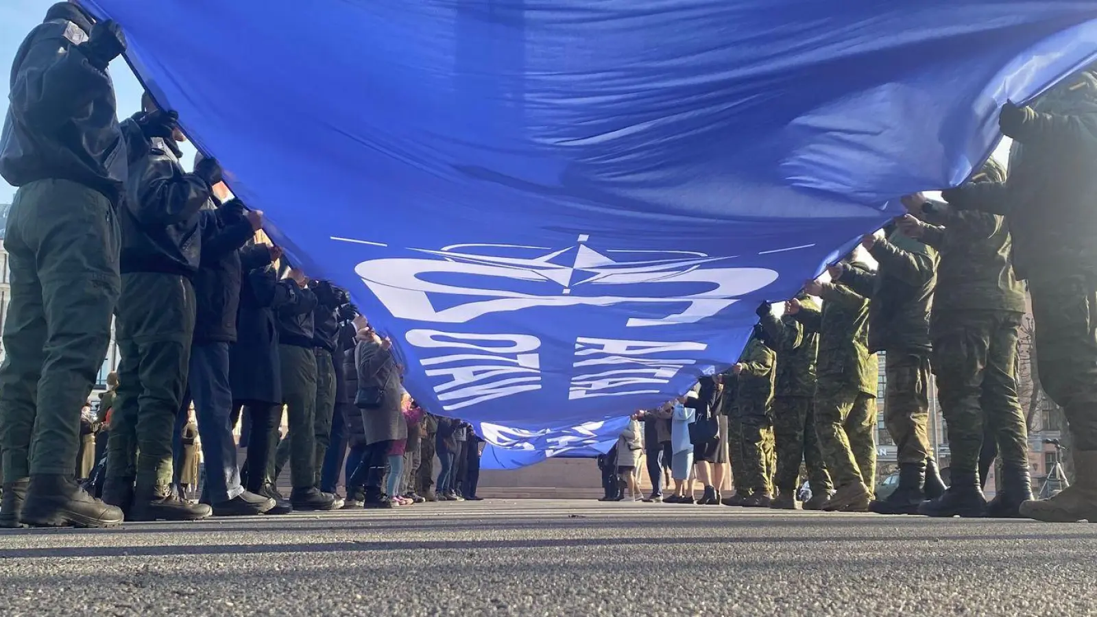 Ein riesige blaue Fahne mit der Aufschrift „Latvija Nato 20“ wird vor dem Freiheitsdenkmal entrollt. Lettland feiert 20 Jahre Nato-Mitgliedschaft. (Foto: Alexander Welscher/dpa)