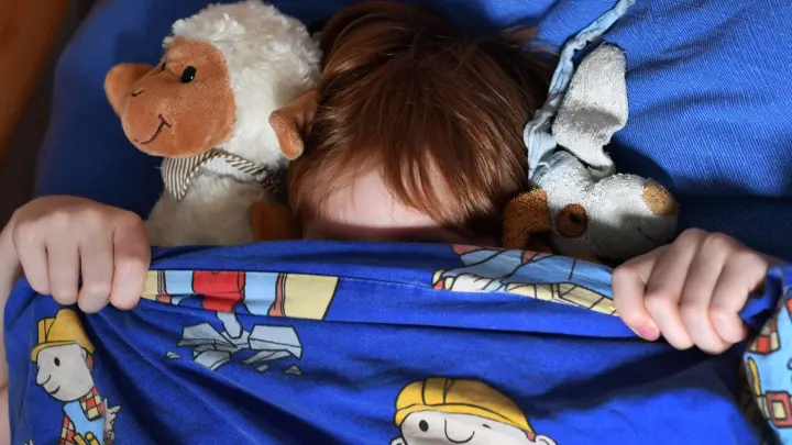 Ein Junge zieht sich vor Angst die Bettdecke über das Gesicht. In einem Kinderbuch geben mitunter Thomas Müller und Rolf Zuckowski Tipps gegen Ängste und Sorgen. (Foto: Jens Kalaene/dpa-Zentralbild/dpa)