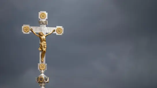 Ein katholisches Kruzifix ist vor dunklen Wolken zu sehen. (Foto: Marijan Murat/dpa/Symbolbild)
