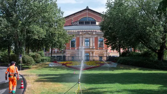 Ein städtischer Mitarbeiter bewässert die Grünfläche vor dem Festspielhaus in Bayreuth. (Foto: Daniel Vogl/dpa/Archivbild)