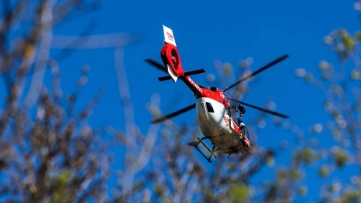 Ein Helikopter der DRF Luftrettung schwebt am Himmel über einem Waldstück. Für eine zügige und schonende Rettung aus unzugänglichen Gebieten ist der Hubschrauber mit einer fest installierten Winde ausgestattet. (Foto: Philipp von Ditfurth/dpa)