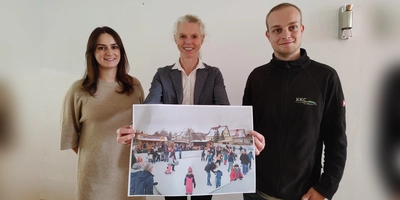 Daniela Übler, Birgit Grübler und Jochen Schauer (von links) zeigen ein Foto der Schlittschuhbahn. Diese wird beim Weihnachtsmarkt heuer erstmals am Bad Windsheimer Marktplatz stehen. (Foto: Katrin Merklein)