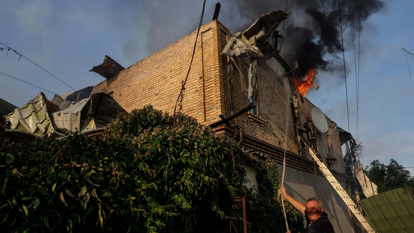 Ein Anwohner löscht ein Feuer in einem Haus, das nach russischem Beschuss in Cherson, Ukraine, beschädigt wurde. (Foto: Evgeniy Maloletka/AP/dpa)