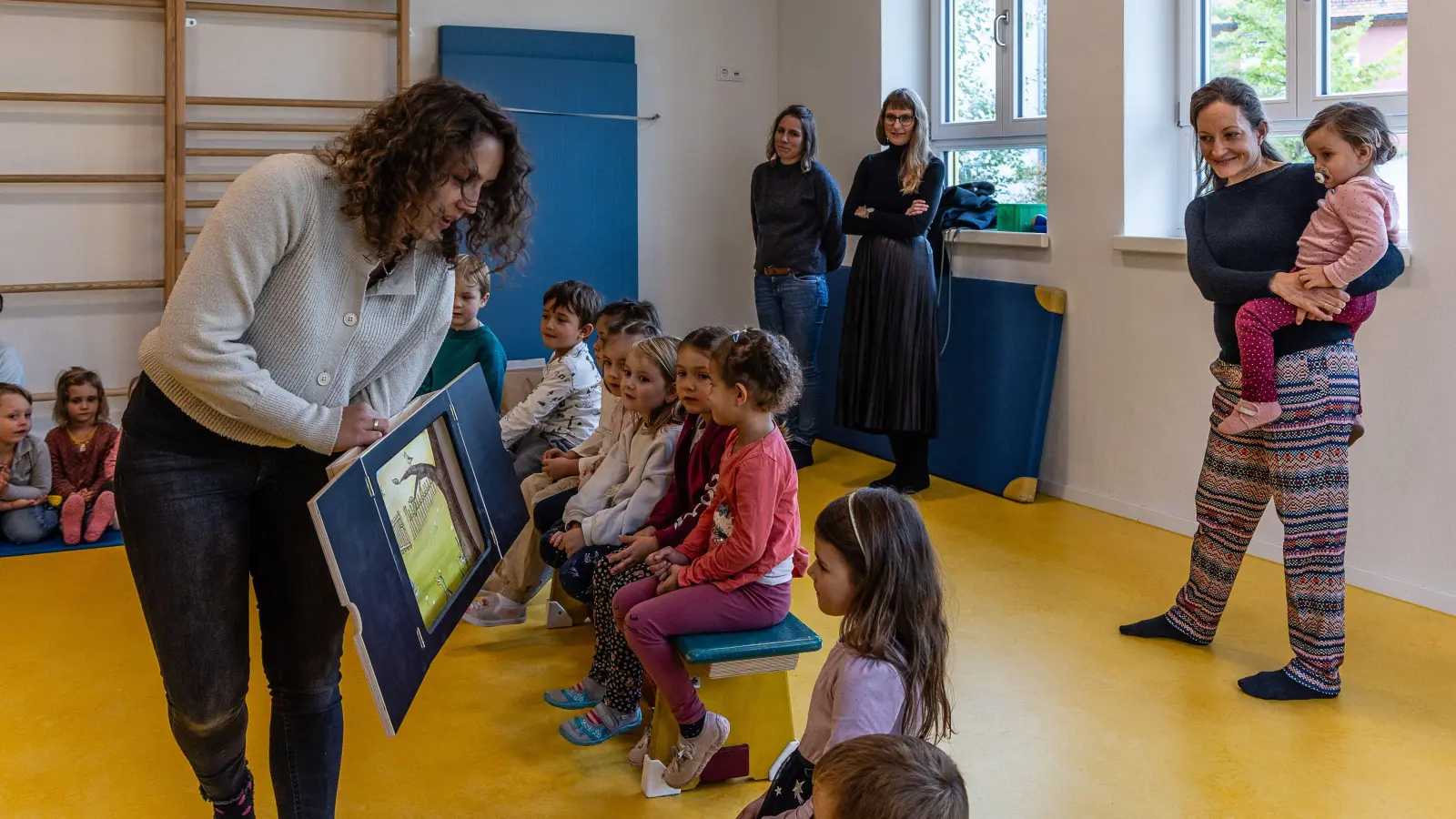 Die Musikpädagogin Teresa Spors erzählt den Kindern den Inhalt des Märchens „Peter und der Wolf“, als Zuhörerinnen sind (von rechts) Christiane Karg, Dr. Maria Wüstenhagen (Leiterin des Kulturbüros), Miriam Kälberer und die Kinder und Erzieherinnen des Kindergartens mit dabei. (Foto: Günter Schmidt)