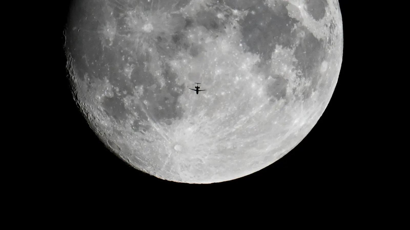 Ein Passagierflugzeug fliegt am Abend scheinbar auf den zunehmenden Mond zu. (Foto: Arne Dedert/dpa)